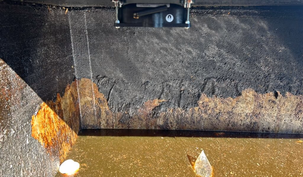 A dirty container, with rust and residue on the walls and a sensor mounted above.