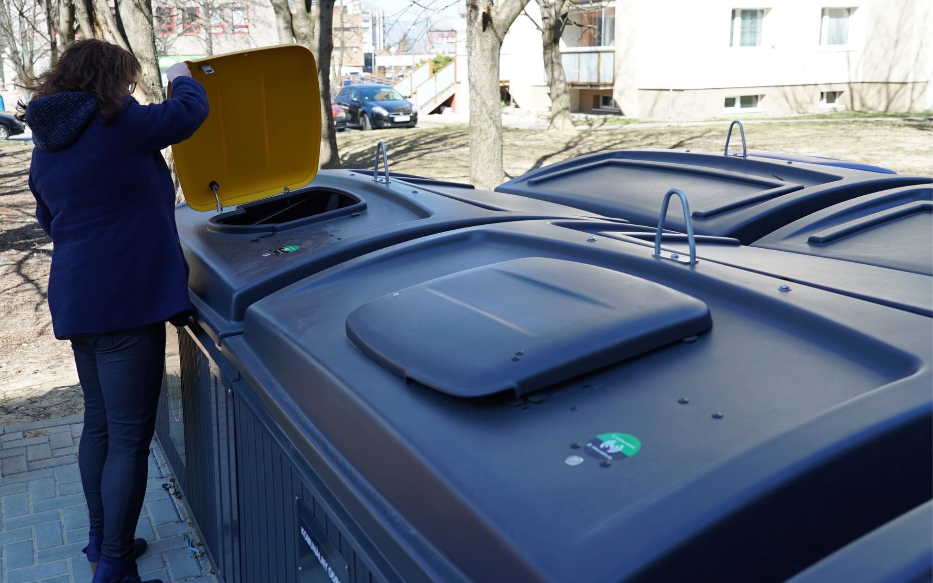 A person opening a waste bin with a yellow lid.