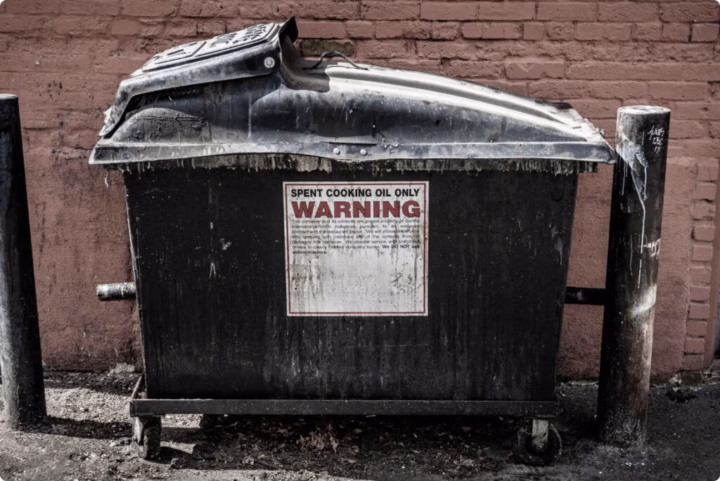 A waste container with a warning label stating "Spent Cooking Oil Only," next to a wall.