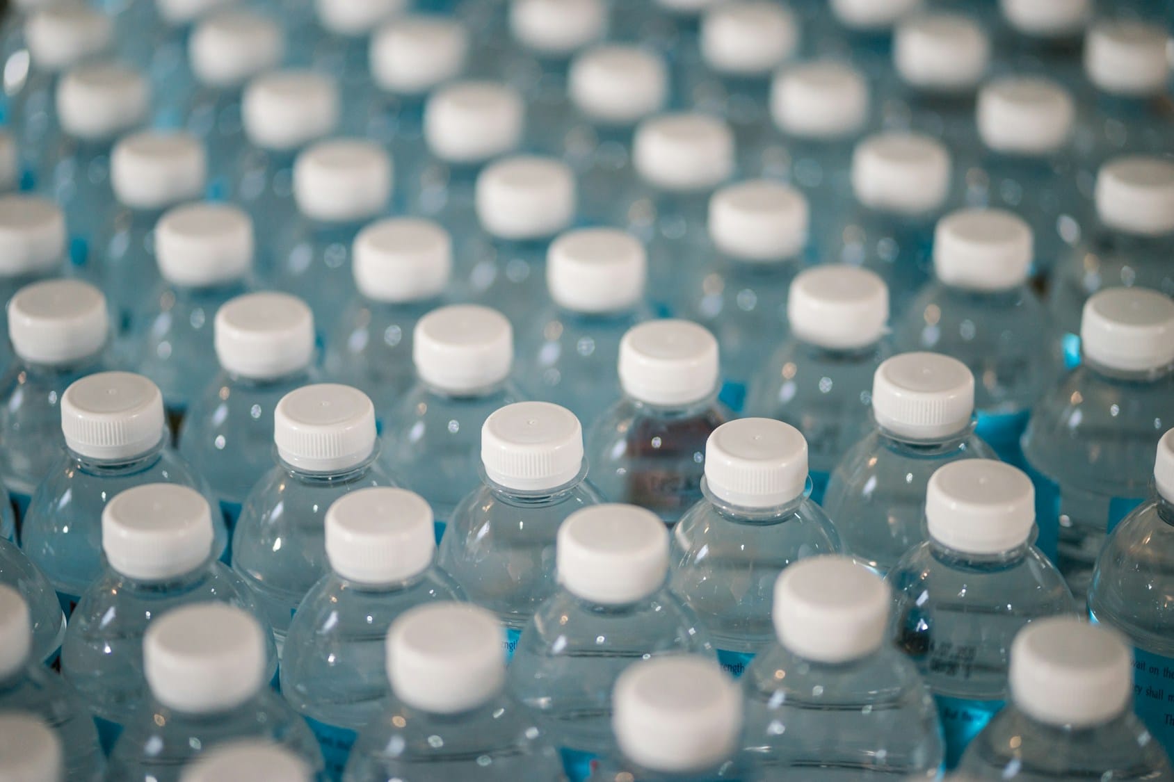 Numerous plastic water bottles with white caps arranged in a grid.