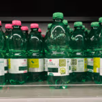 Green plastic water bottles with pink and green caps are neatly arranged on a store shelf.