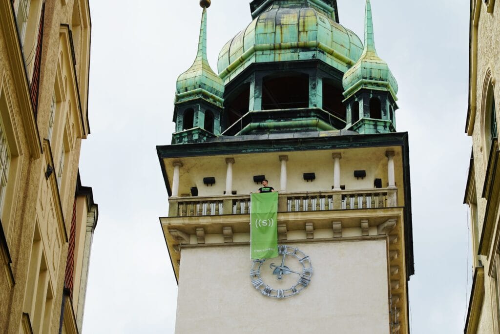 A person hanging a green banner from a tower with a clock in the background.