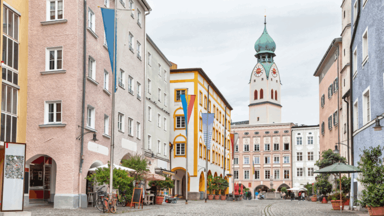Colorful historic buildings line a cobblestone street with cafés and a tall clock tower.
