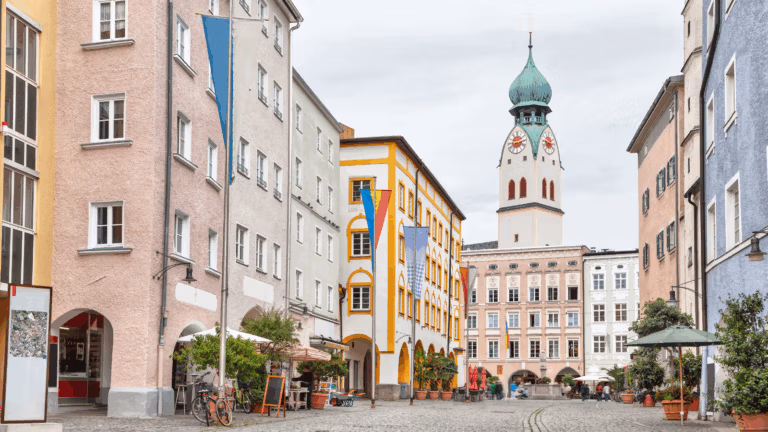 Colorful historic buildings line a cobblestone street with cafés and a tall clock tower.