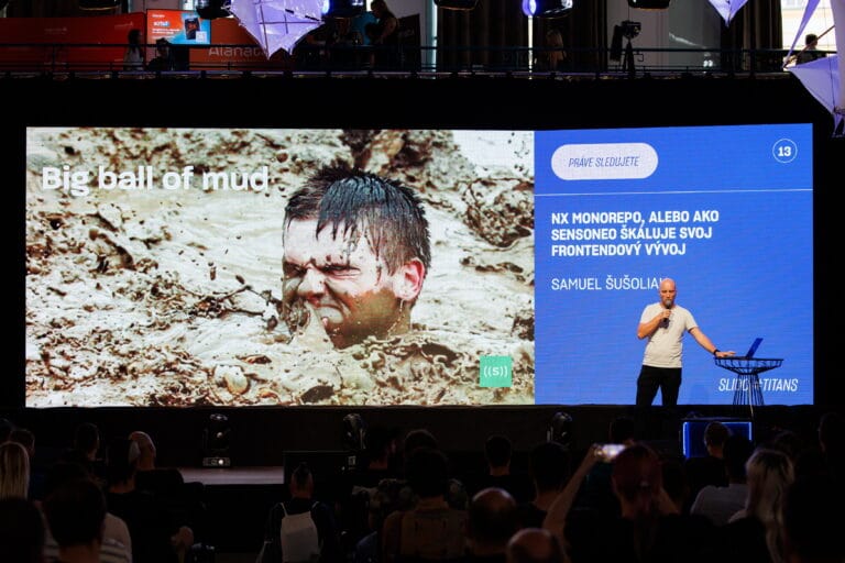 Speaker presenting on stage in front of a large screen to an audience.