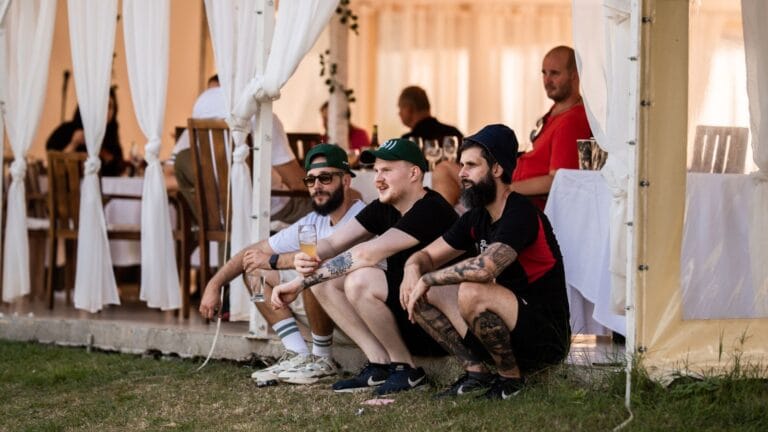 A small group sits outside a tent, relaxing with drinks and watching an event.