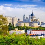 A bright view of Madrid featuring the Royal Palace and Almudena Cathedral above lush greenery.