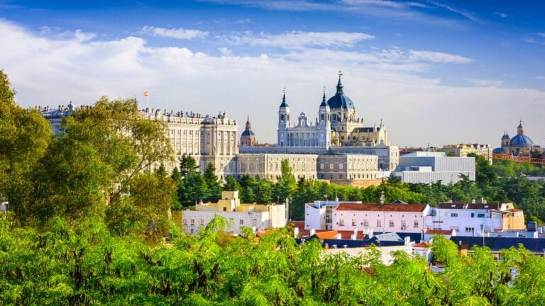A bright view of Madrid featuring the Royal Palace and Almudena Cathedral above lush greenery.