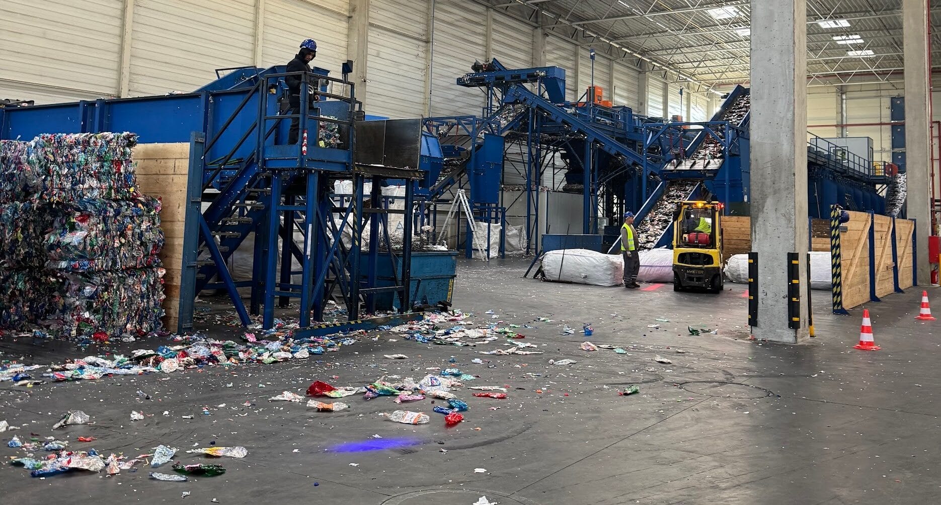 Plastic recycling facility with conveyor machinery, baled plastics, and workers sorting waste.