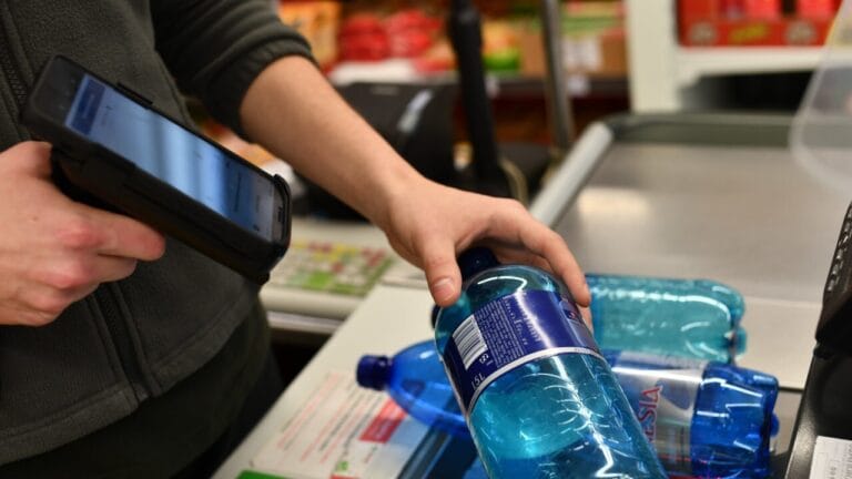 A person scans plastic bottles at a checkout or recycling station using a handheld device.