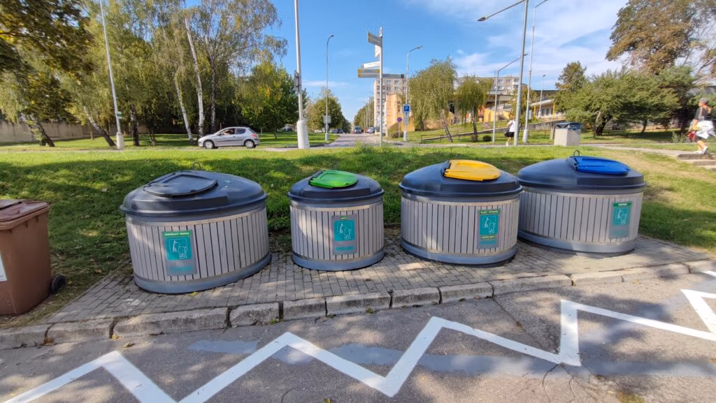Group of large outdoor semi-underground recycling containers with color-coded lids for sorted waste.