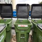 Three open green recycling bins with sensors inside the lids to monitor fill levels.