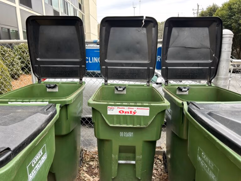 Three open green recycling bins with sensors inside the lids to monitor fill levels.