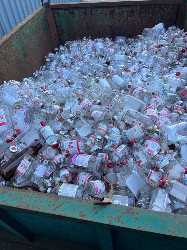 Large metal container filled with discarded glass bottles.
