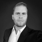 Man in a suit posing confidently against a dark, neutral background.