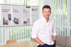 Man in a white shirt smiling in a bright office setting.