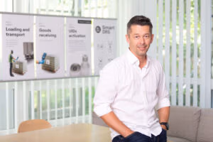 Man in a white shirt smiling in a bright office setting.
