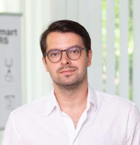 Man in glasses wearing a white shirt, looking at the camera with a neutral expression.