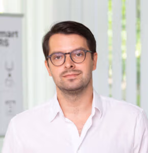 Man in glasses wearing a white shirt, looking at the camera with a neutral expression.