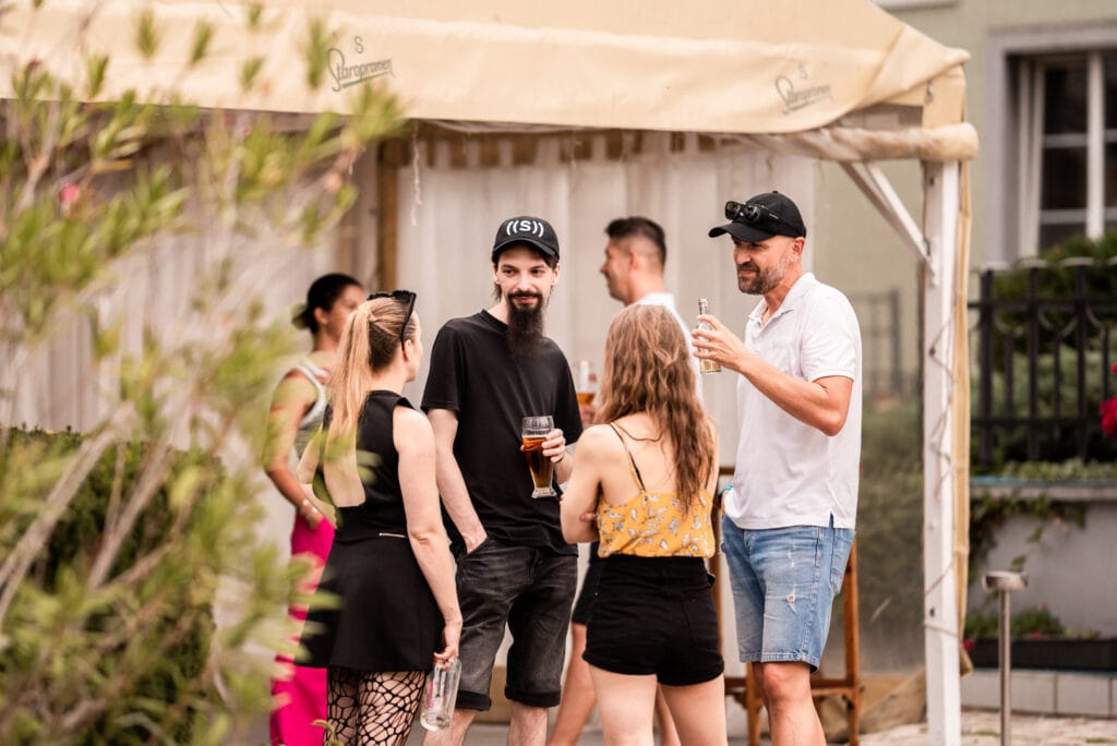 A group of people chatting and enjoying drinks at an outdoor gathering under a tent.
