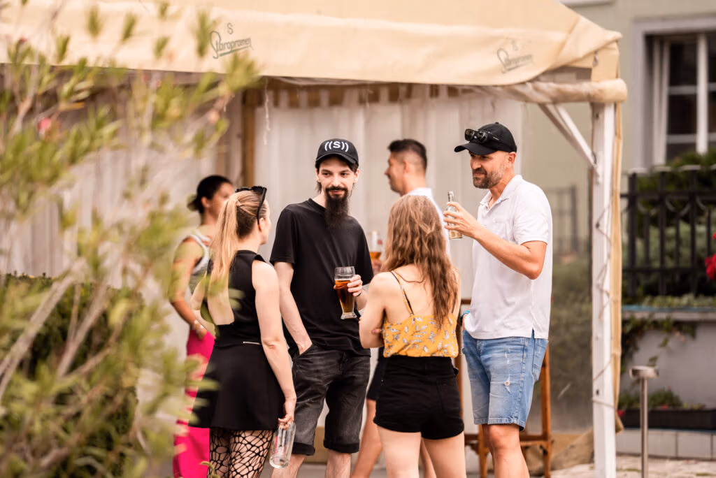 A group of people chatting and enjoying drinks at an outdoor gathering under a tent.