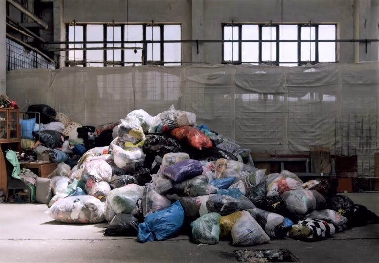 Large pile of bagged textiles and waste stored indoors, awaiting sorting or disposal.