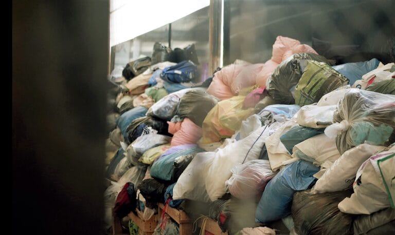 A large pile of tightly packed bags filled with donated clothing inside a collection facility.