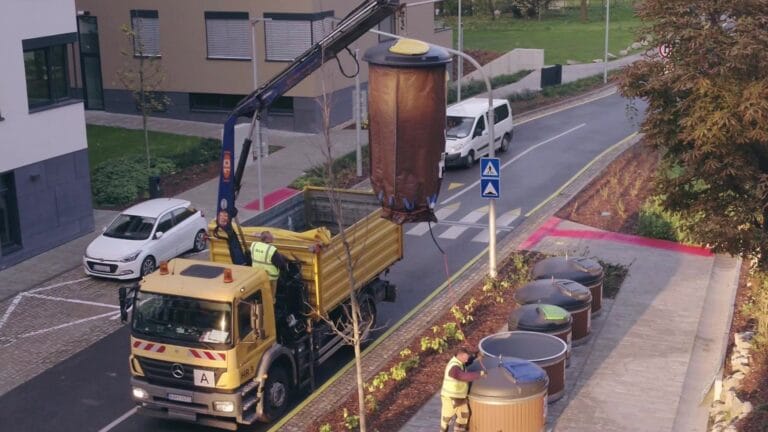 Waste collection truck using a crane to empty semi-underground bins.
