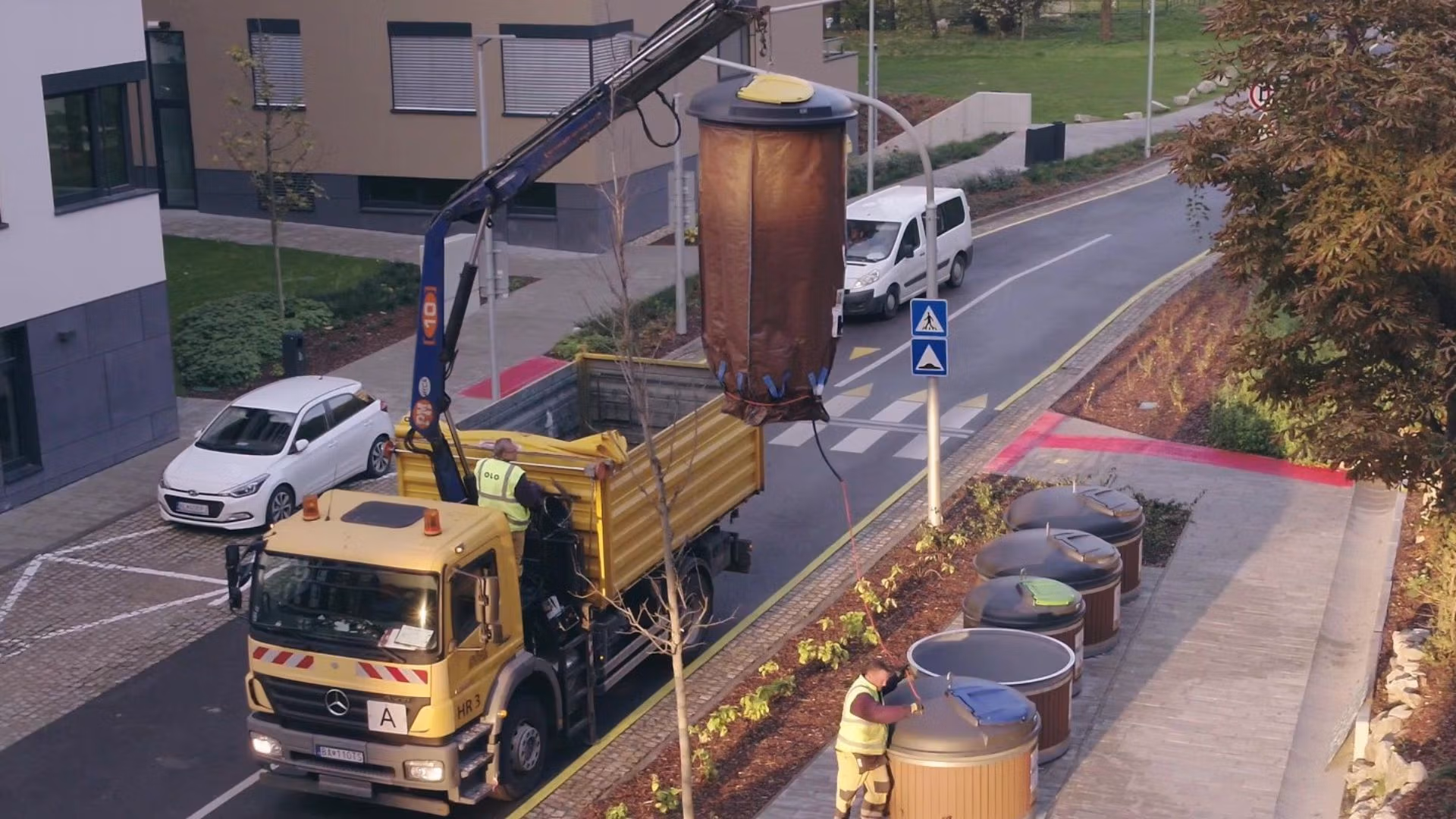 Waste collection truck using a crane to empty semi-underground bins.