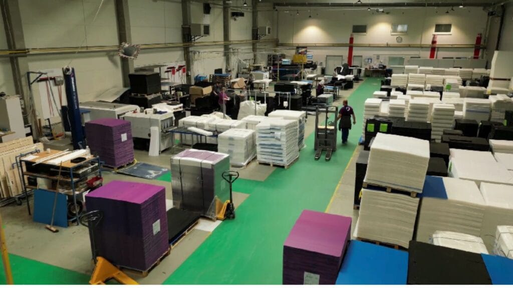 A busy production floor with stacked materials and workers moving equipment.
