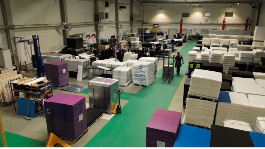 A busy production floor with stacked materials and workers moving equipment.