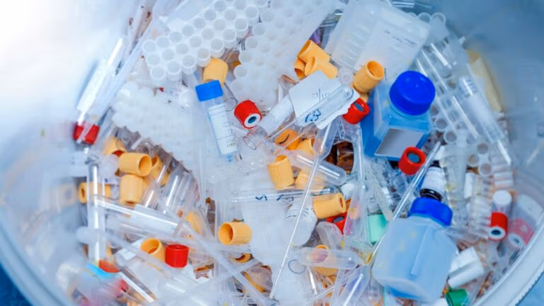 Container filled with discarded lab plastics, test tubes, caps, and sample vials.