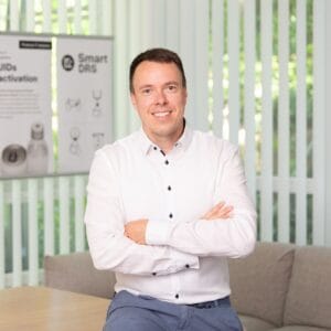 A man in a white shirt smiling, photographed indoors in a bright, professional setting.
