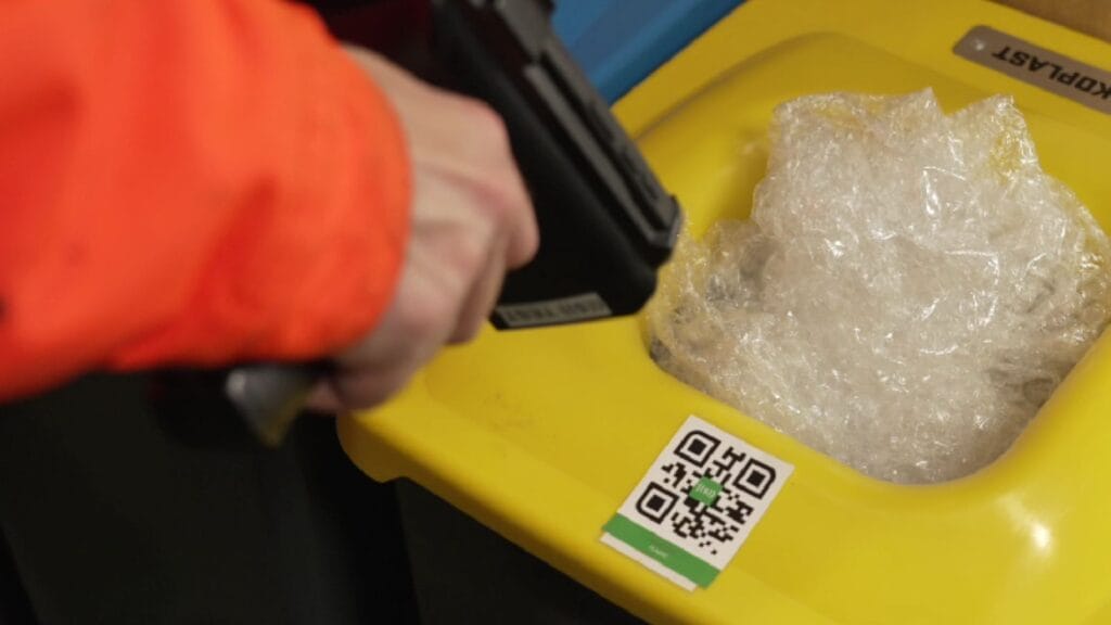 Worker scanning a QR code on a recycling bin filled with plastic.
