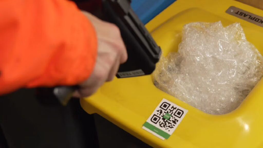 Worker scanning a QR code on a recycling bin filled with plastic.