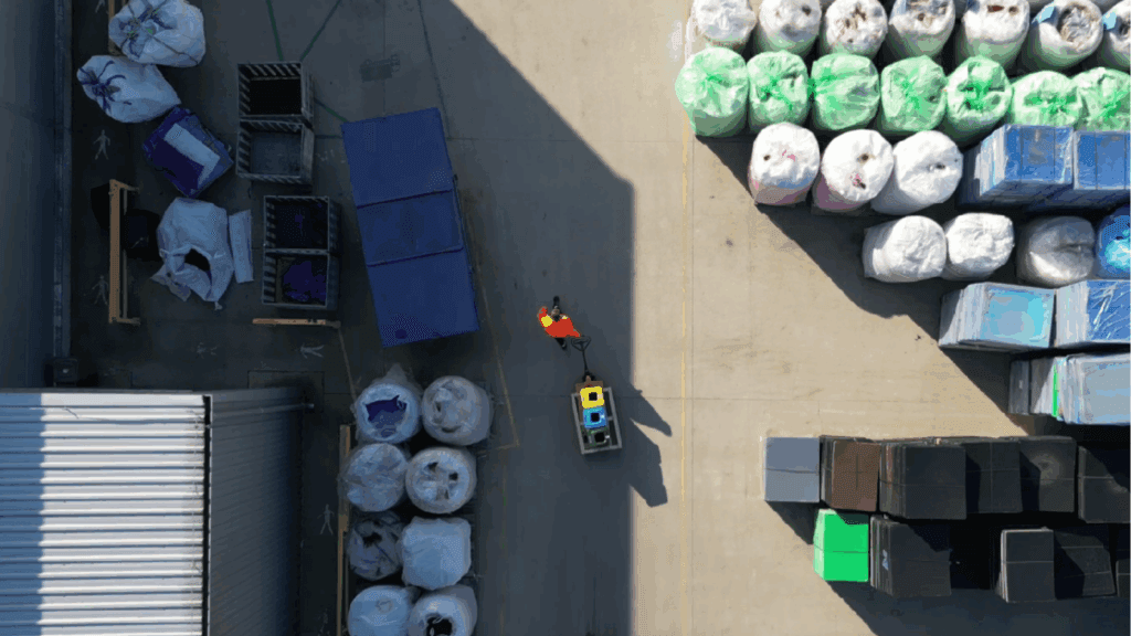 Worker moving small recycling bins through an industrial yard with sorted waste.

