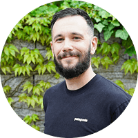 Smiling man outdoors with a leafy green wall background.