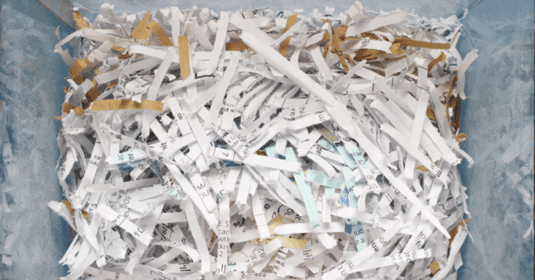 Shredded paper scraps mixed with bits of tape, filling a container after document destruction.