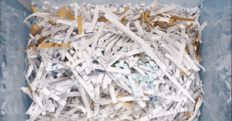 Shredded paper scraps mixed with bits of tape, filling a container after document destruction.