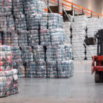 Warehouse filled with stacked compressed bales while a forklift moves materials through the aisle.