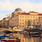 Waterfront city with historic buildings, boats and street activity.