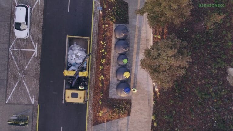 Aerial view of a waste collection truck emptying underground smart bins on an urban street.