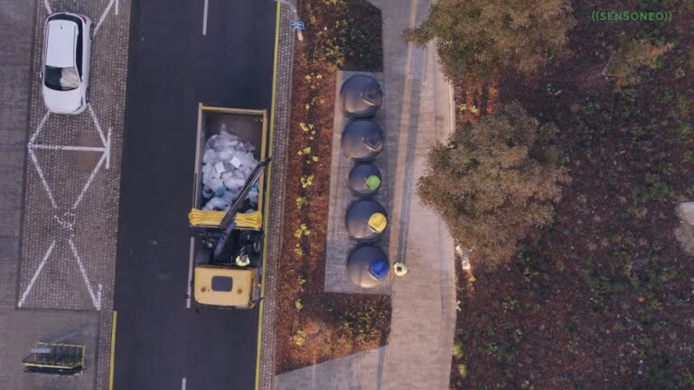 Aerial view of a waste collection truck emptying underground smart bins on an urban street.