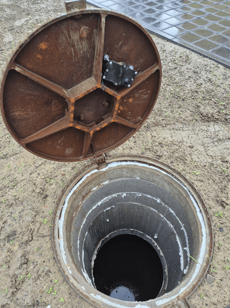 Black sensor unit bolted to the underside of the manhole cover.