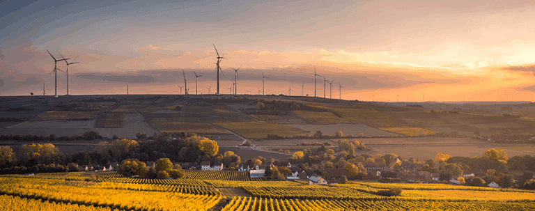 Wind turbines overlooking farmland at sunset.
