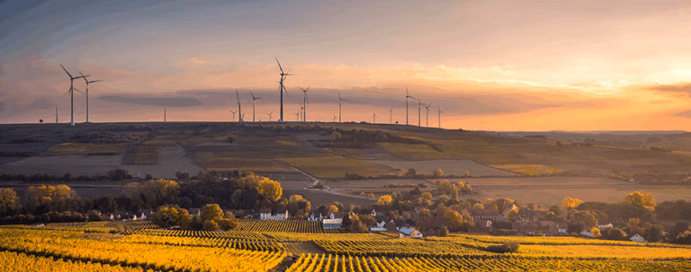 Wind turbines overlooking farmland at sunset.