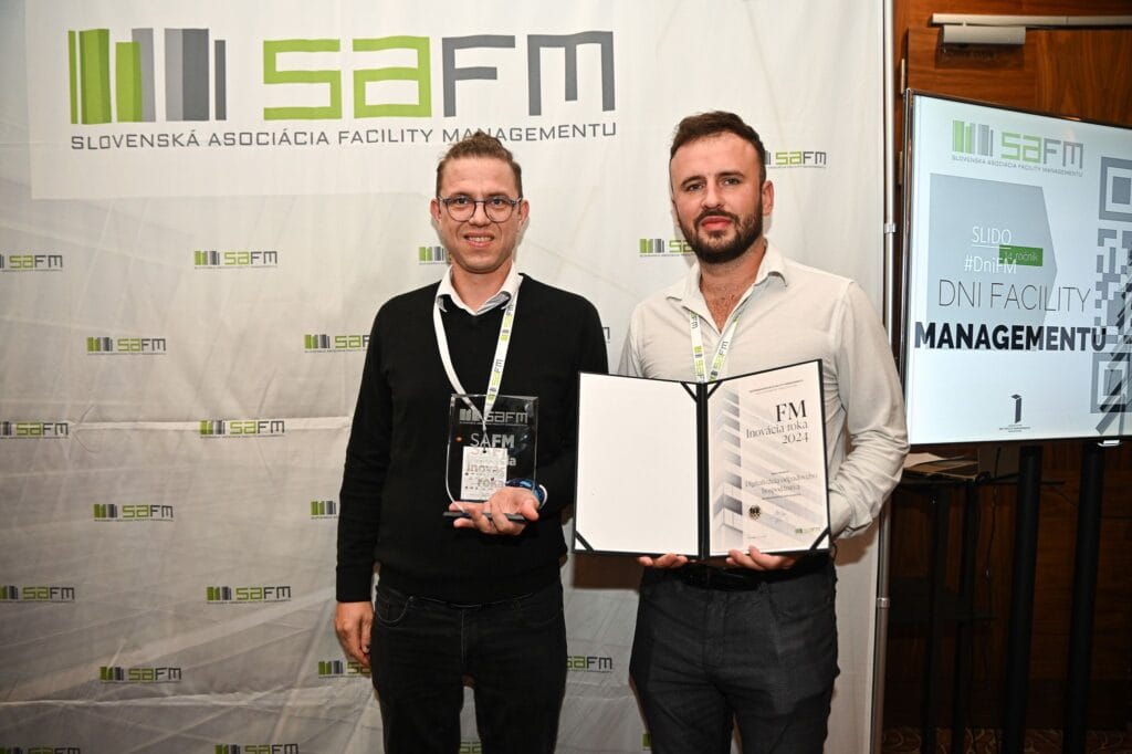 Two men proudly presenting an award certificate and trophy at a professional facility-management event.
